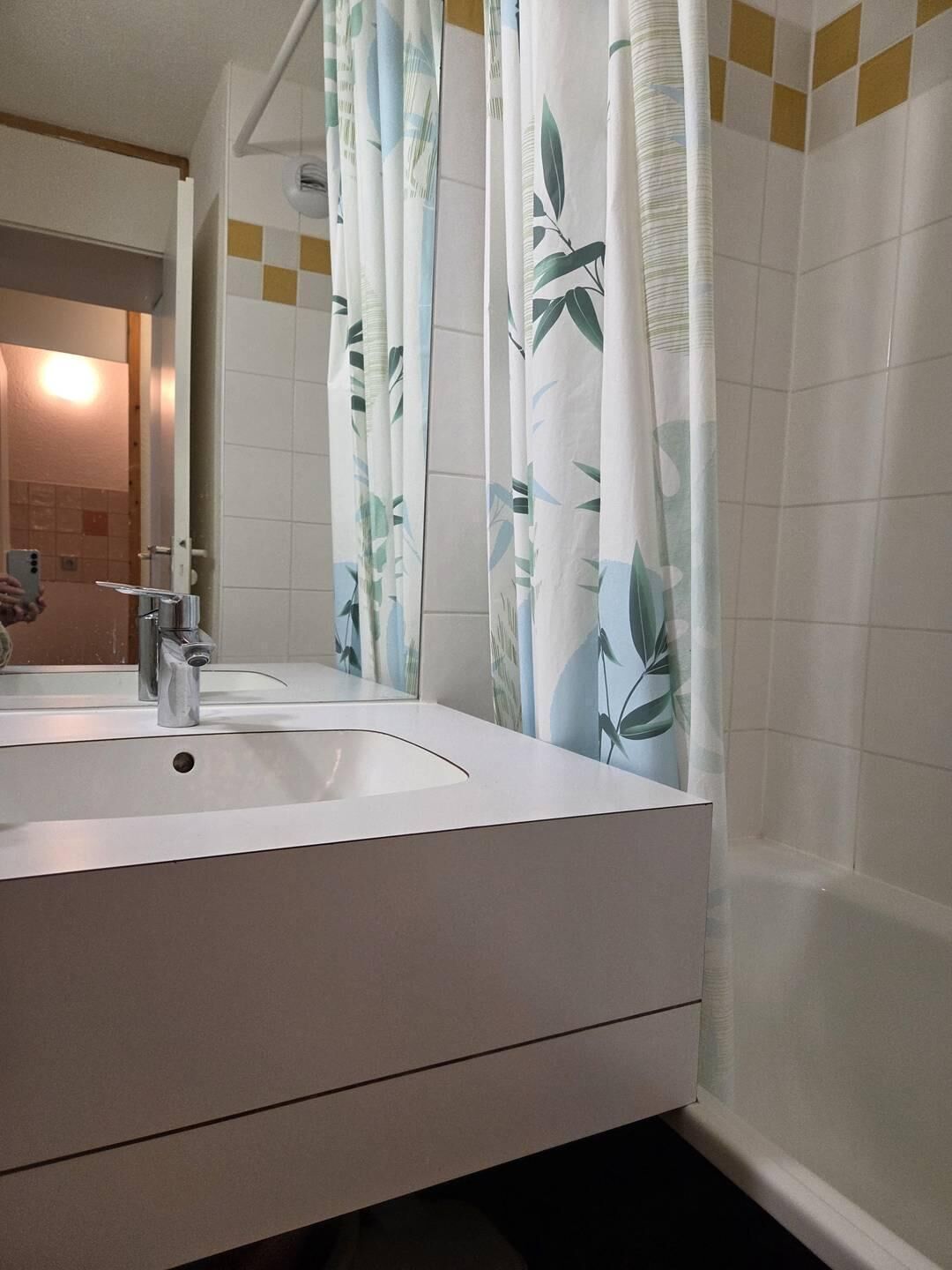 A bathroom with a white sink, a mirror, and a shower curtain with a leaf pattern.