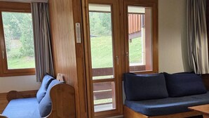 Ett rum med en träbänk och en soffa, stora fönster och utsikt över grönområden utanför.