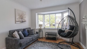 Ett modernt vardagsrum med en grå soffa, en hängstol, en mönstrad matta och ett fönster med persienner.