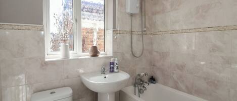 Une salle de bain avec des toilettes, un lavabo et une baignoire. Il y a une fenêtre donnant sur des arbres et un mur de briques.