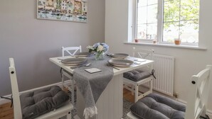 En matplats med ett bord dukat för fyra personer, vita stolar, ett fönster med utsikt över grönområden och en tavla på väggen.