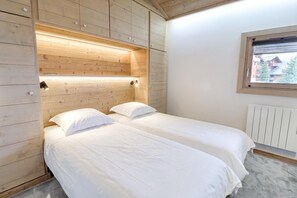 A bedroom with two beds, wooden paneling, a window, and a radiator.
