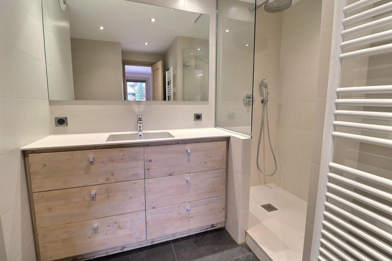 Une salle de bain moderne avec un meuble-lavabo en bois, un grand miroir, une douche avec une paroi en verre et un porte-serviettes blanc.