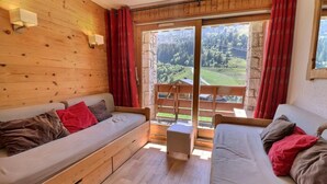 Ein gemütliches Zimmer mit Holzvertäfelung, einer Couch, einem Bett und Blick auf eine grüne Landschaft durch eine Glastür.