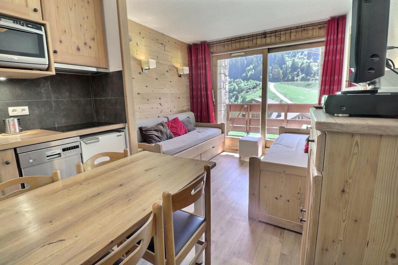 A compact kitchen with modern appliances, a dining area with wooden furniture, and a cozy seating area with a view of the outdoors.