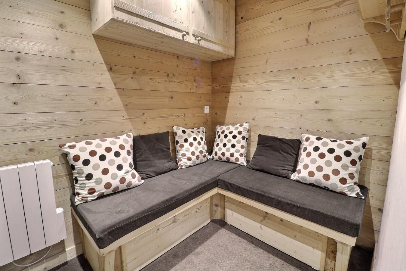 Un canapé d’angle avec des coussins à pois, un plafond en bois et un radiateur blanc.