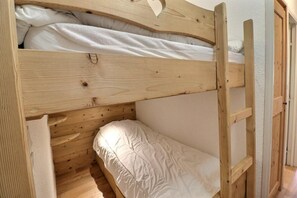 Ein Etagenbett mit Holzleiter, weißer Bettwäsche und einem kleinen Fenster.