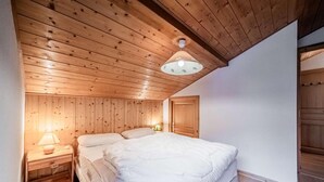 Une chambre avec des murs lambrés en bois, un grand lit, une table de chevet avec une lampe et un luminaire au plafond.