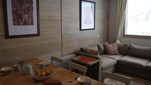 Una sala de estar acogedora con pared de madera, un sofá, una mesa de comedor con un tazón de fruta y cuadros enmarcados.