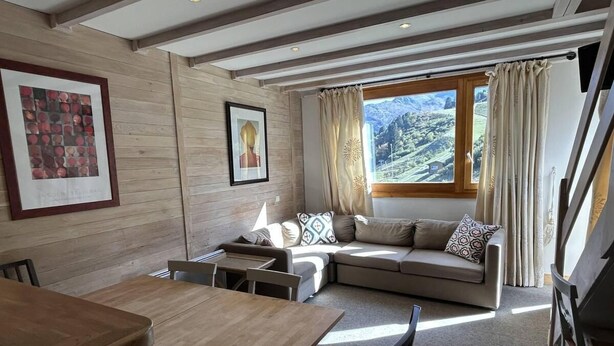 Una sala de estar acogedora con un sofá, una mesa de comedor y una ventana con cortinas.