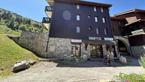 Edificio de dos pisos con fachada de piedra y sección superior oscura. Cuenta con áreas de estar al aire libre, con mesas y sillas.