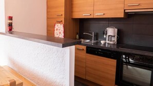 A modern kitchen with wooden cabinets, a black tiled backsplash, a coffee maker, and a dishwasher.