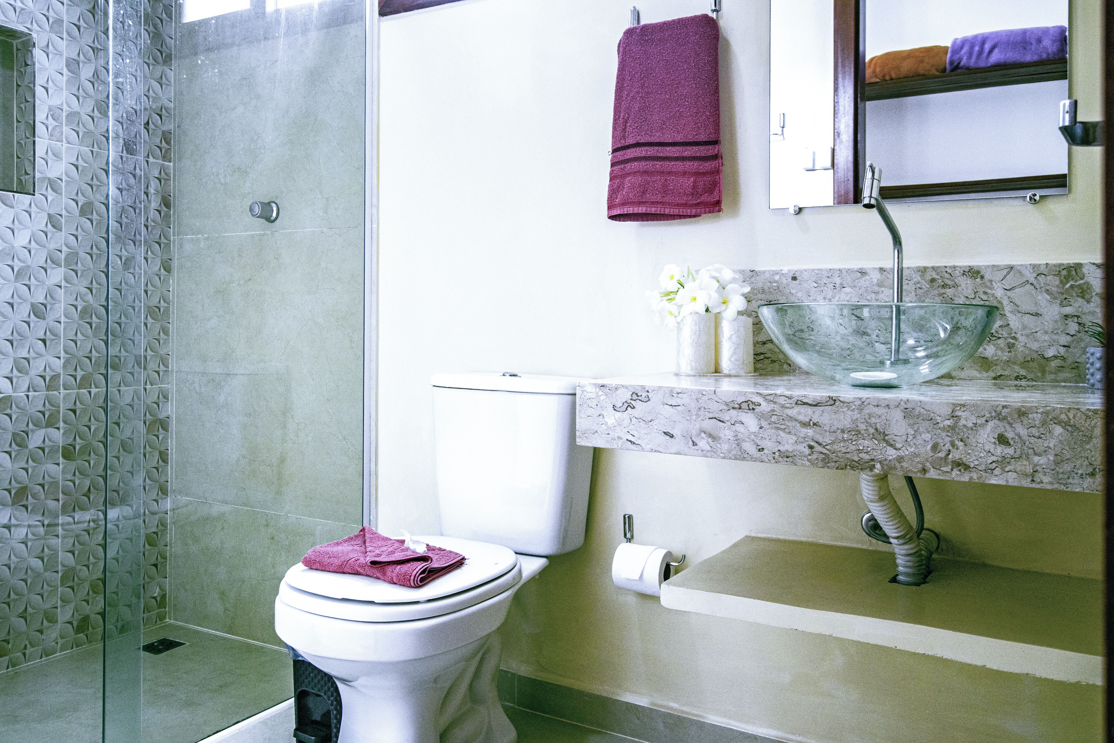 Un baño con cabina de ducha de vidrio, un inodoro, un lavabo con encimera de mármol y un espejo sobre el lavabo.