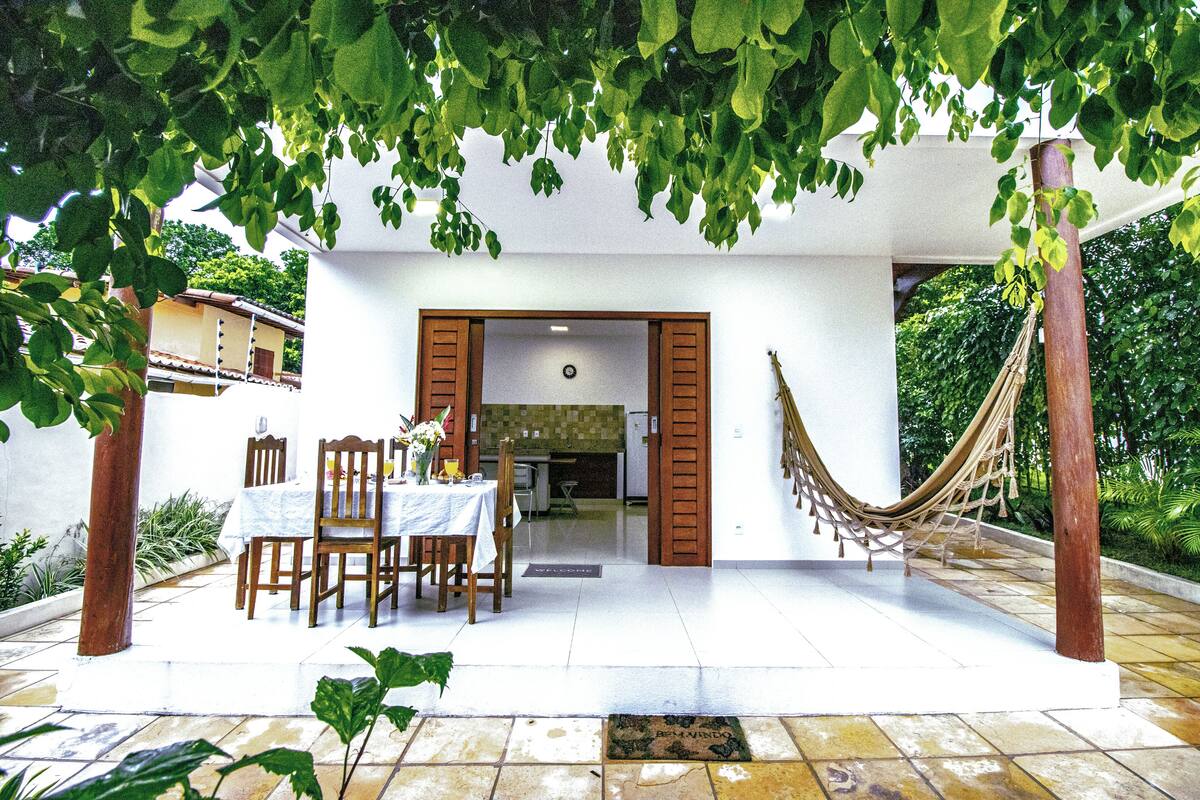 An outdoor patio with a dining table and chairs, a hammock, and a view of the house's interior.