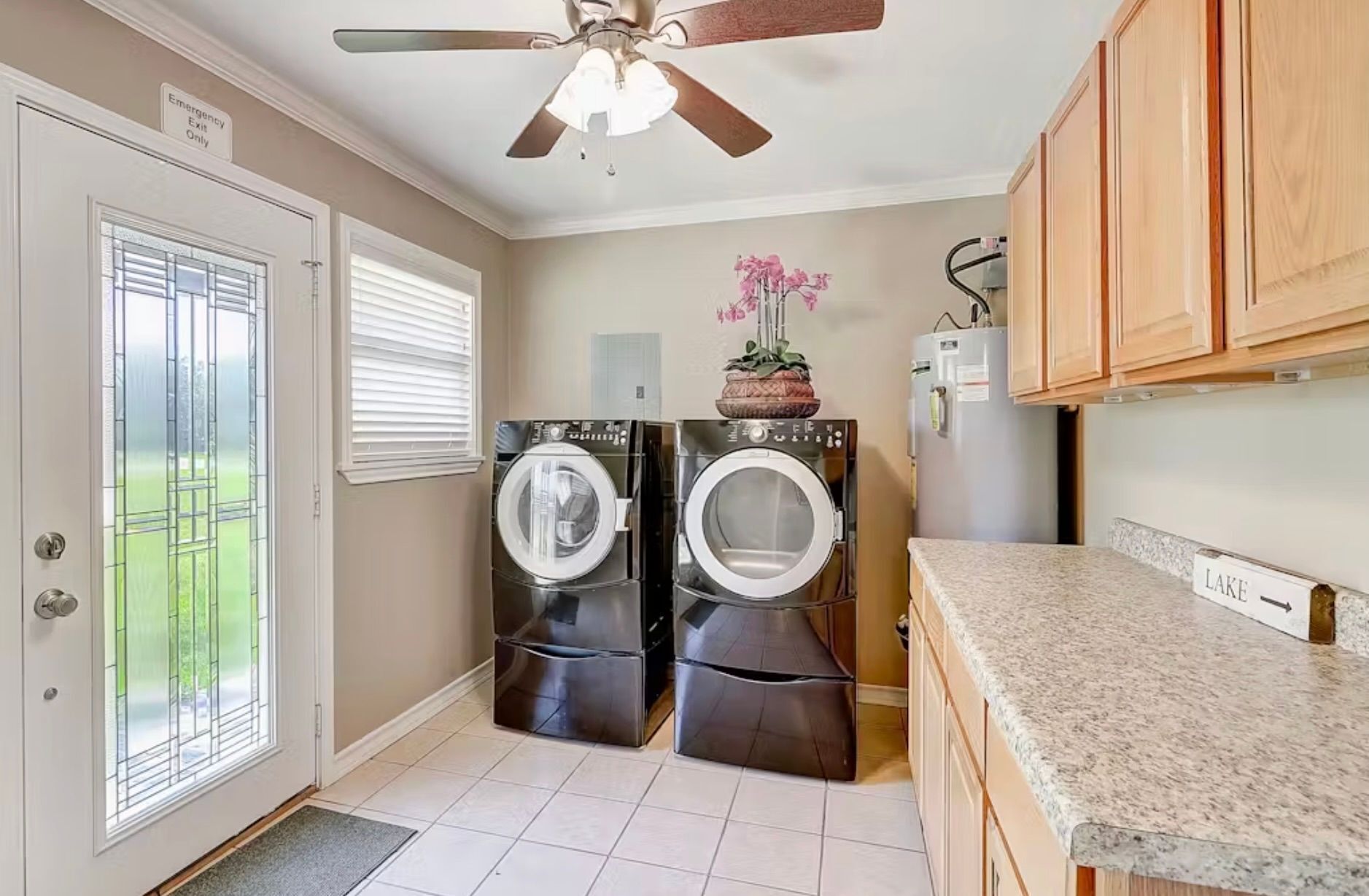 A laundry room with two front-loading washers and dryers, a ceiling fan, a refrigerator, and a countertop.