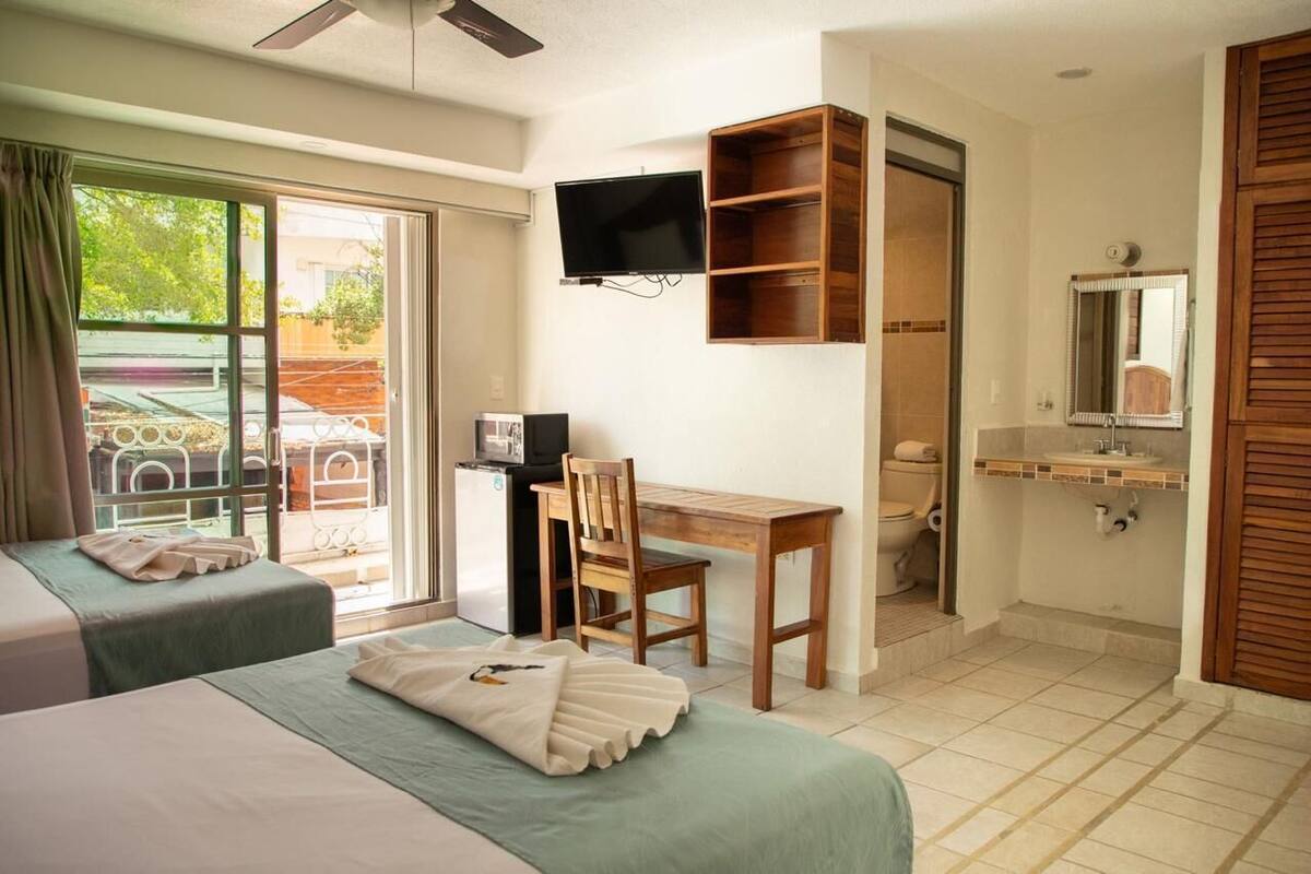 Une chambre avec deux lits, un bureau, une télévision, une salle de bain et une vue sur l’extérieur.