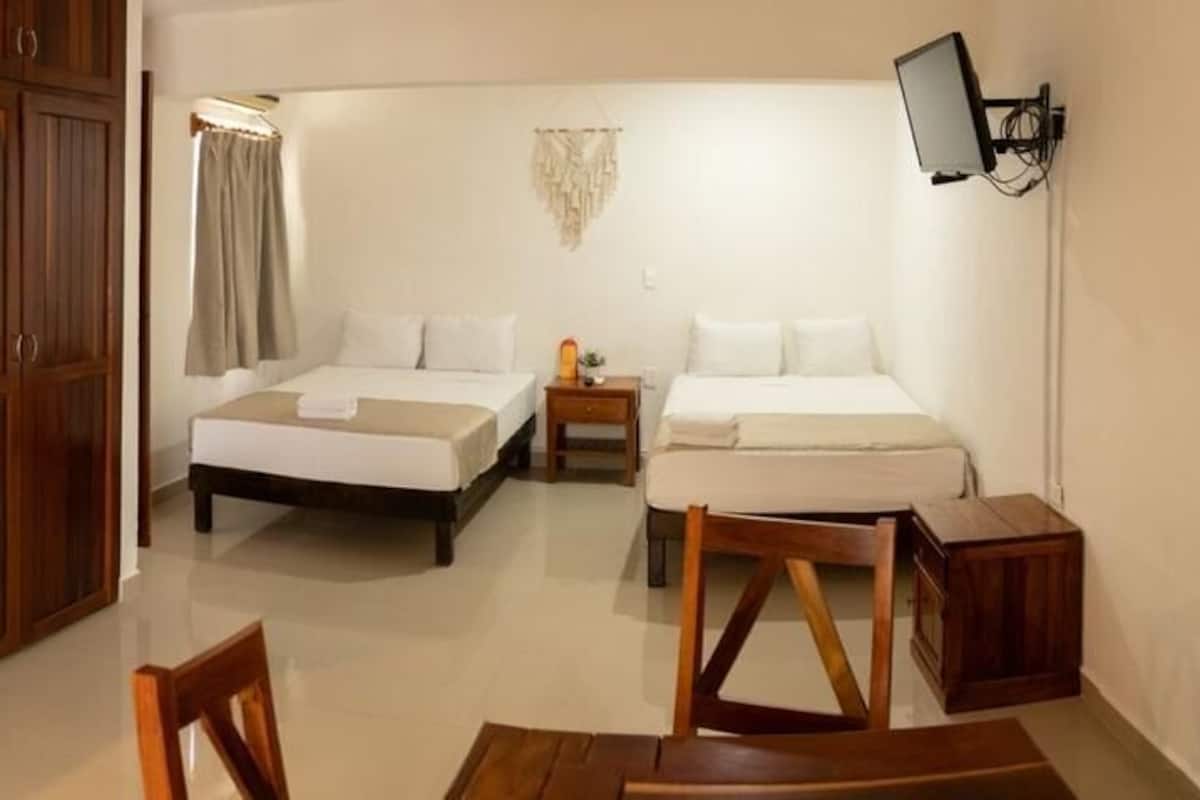 Une chambre d’hôtel compacte comprenant un coin cuisine, un lit, une table de chevet et un téléviseur fixé au mur.
