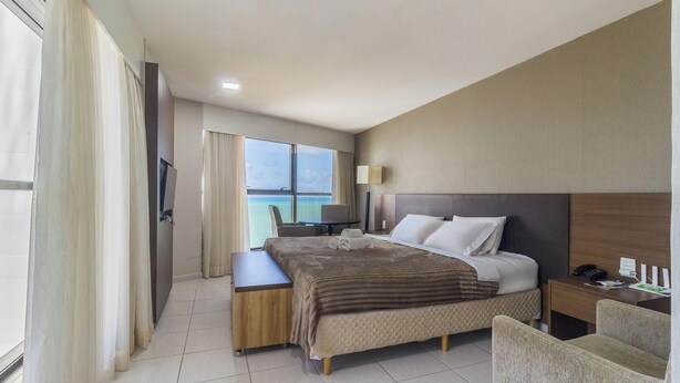 A hotel room with a bed, bedside table, lamp, and a view of the sea. - Estúdio Moderno com Vista Mar em Recife BCI1603 (Recife)