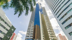 A tall building with multiple floors and a mix of architectural styles, surrounded by other high-rise buildings. - Estúdio Moderno com Vista Mar em Recife BCI1603 (Recife)