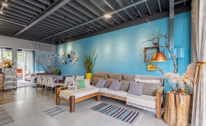 A modern living room with a blue accent wall, a sofa, a coffee table, and a dining area with chairs and a table. - House Near the Beach and Beto Carrero Efp0356 (Penha)
