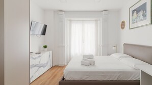 Une chambre d’hôtel avec un lit, un téléviseur fixé au mur, un meuble aux motifs imitant le marbre et une fenêtre avec des rideaux.