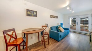 Una sala de estar con una mesa de comedor de madera, dos sillas, un sofá azul y vistas a través de puertas de cristal.