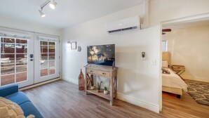 Amplia sala de estar con un televisor grande, piso de madera y puerta corrediza de vidrio que da a un patio exterior.