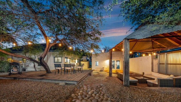 Un espacio al aire libre techado con terraza de madera, asientos e iluminación colgante.