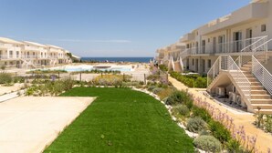 Un hotel con varios balcones, piscina y jardín bien cuidado.