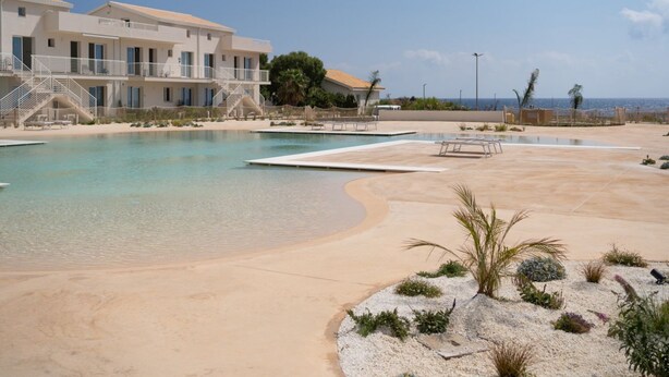Un resort con piscina, zona de playa y un edificio con balcones.