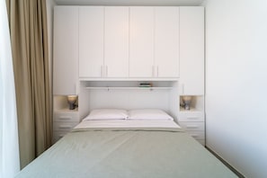 Une chambre à coucher avec un lit, une armoire blanche, des lampes de chevet et une étagère au-dessus du lit.