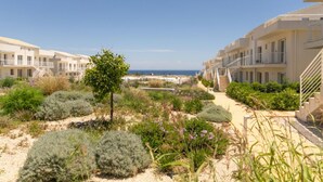 Un hotel frente al mar con edificios de varios pisos, un camino de arena y vistas al océano.