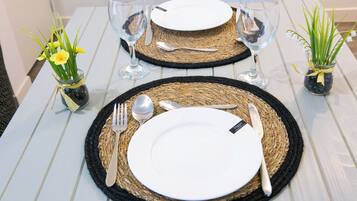 Une table dressée avec de l’argenterie, de la vaisselle blanche et des verres, posée sur une table en bois blanc agrémentée de sets de table en fibres tressées.