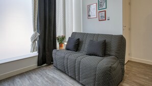 A modern living room with a patterned sofa, a potted plant, and framed artwork on the wall. - Le Pied-à-Terre - Wifi - Centre-ville (Laval)