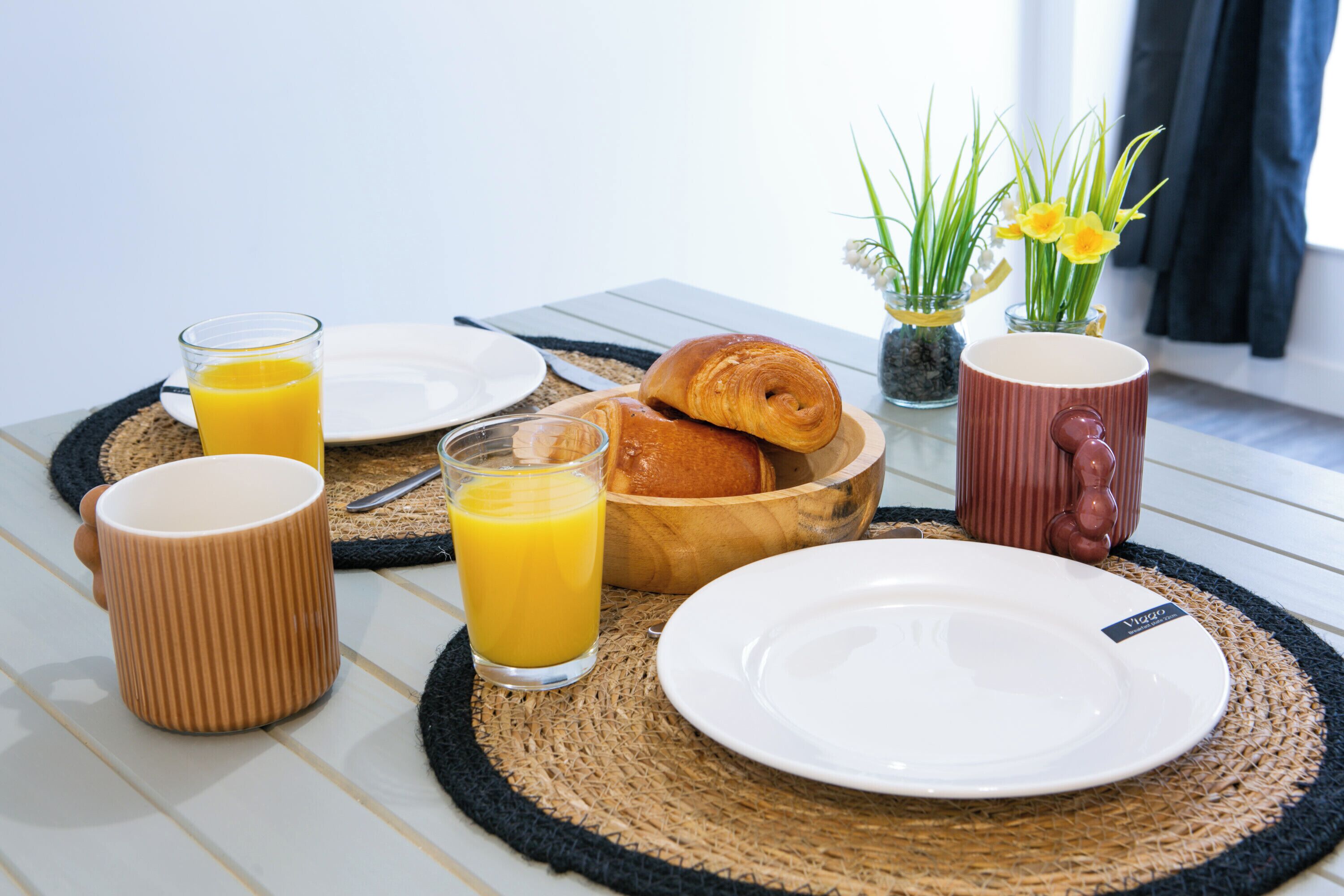Un desayuno con un croissant, jugo de naranja y una taza sobre un posavasos tejido.