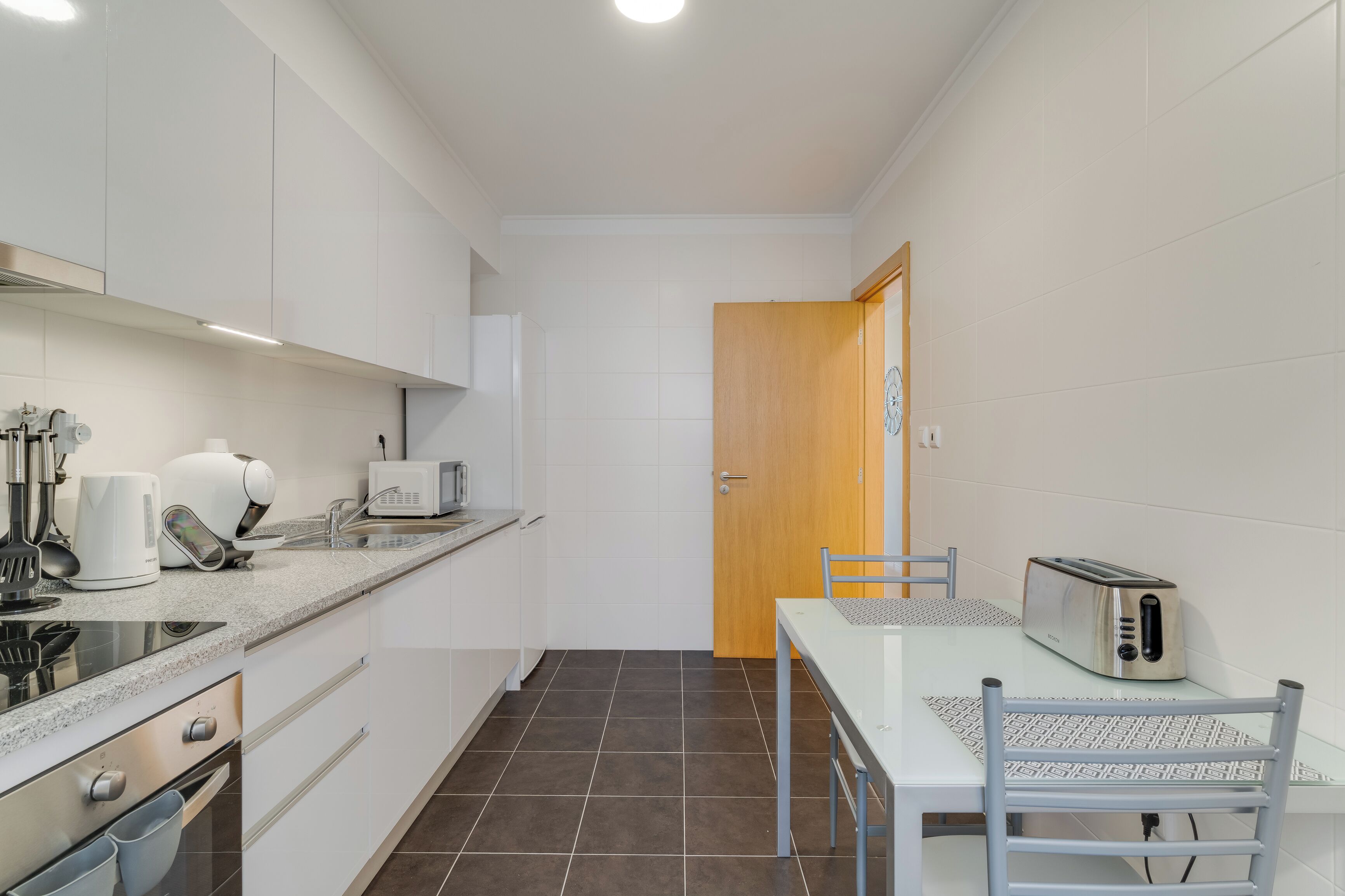 A compact kitchen with white cabinets, a microwave, a toaster, and a small dining table with a chair.