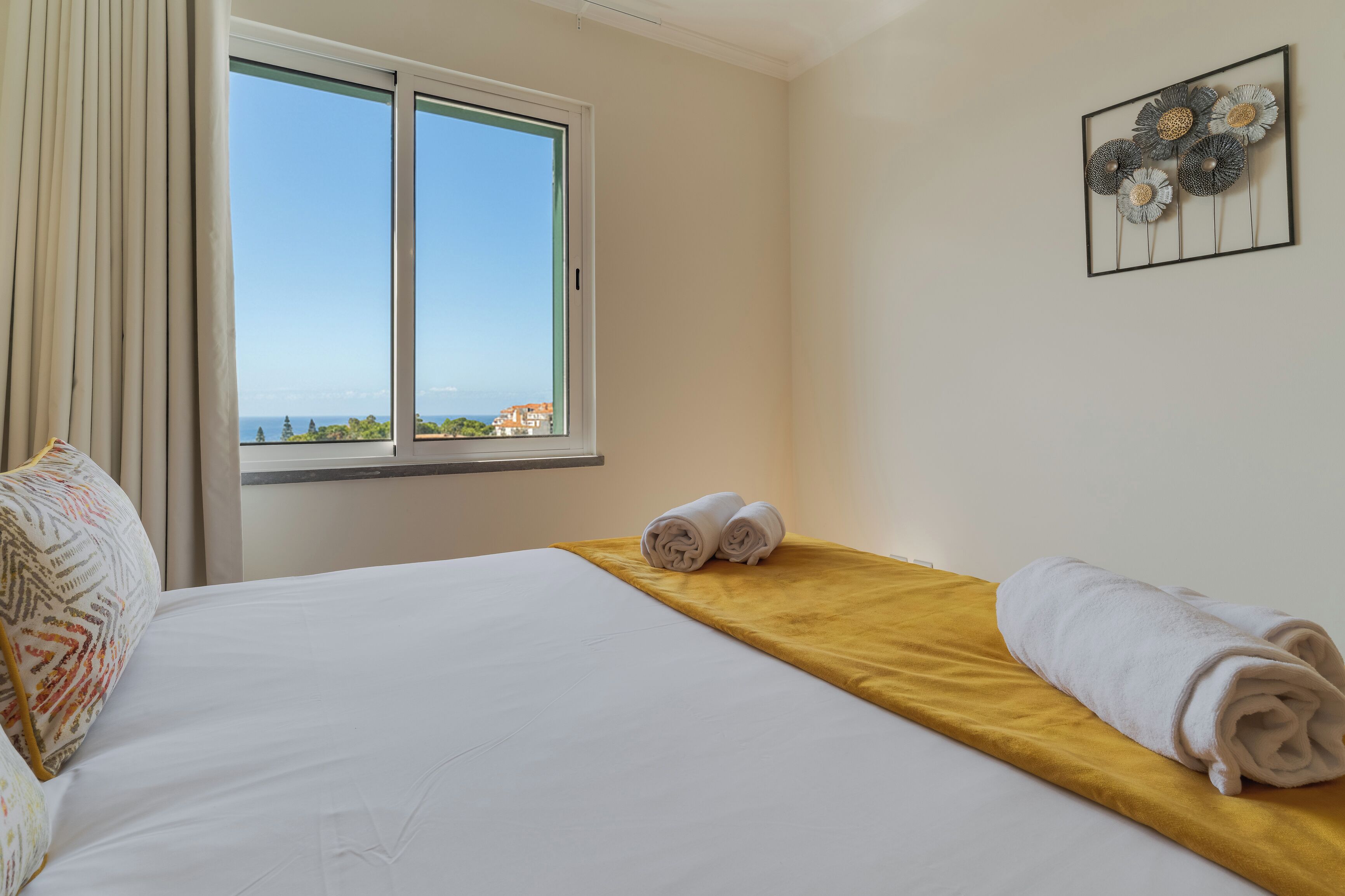 A hotel room with a bed, a window with a view, and a wall art piece.