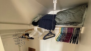 Et lille, kompakt værelse med køjeseng, ventilator, radiator og et tøjstativ med bøjler.