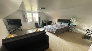 Et soveværelse med seng, fjernsyn, sofa, lille bord og lampe.