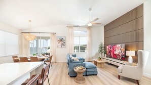 A modern living room with a sofa, armchairs, a dining area, and a television. - Stunning 4-Bed, 3-Bath Pool Home – Just Minutes from Orlando’s Theme Parks (Davenport)