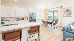 A modern kitchen with white cabinets, a stainless steel refrigerator, and a dining area with a table and chairs. - Stunning 4-Bed, 3-Bath Pool Home – Just Minutes from Orlando’s Theme Parks (Davenport)