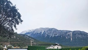 A swimming pool with lounge chairs, a mountain backdrop, and a house in the distance.