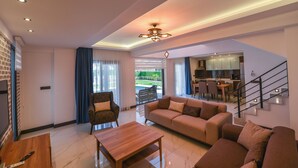 A modern living room with a sofa, armchair, and coffee table. There is a staircase leading to a kitchen area.