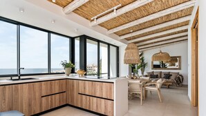 Eine moderne Küche mit großen Fenstern, einem Essbereich mit Tisch und Stühlen und Blick aufs Meer.