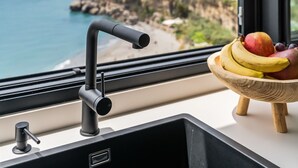 Eine Küche mit einem modernen Wasserhahn, einer Obstschale auf der Arbeitsplatte und Meer- und Stadtblick durch ein Fenster.