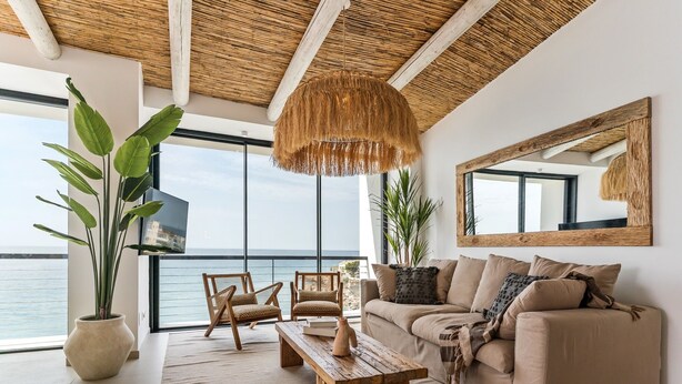 Ein modernes Wohnzimmer mit großem Fenster, einer Couch, zwei Sesseln, einem Couchtisch aus Holz und einer Pendelleuchte.
