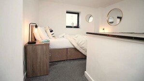 Quarto com cama, mesa de cabeceira, abajur e duas espelhos fixados na parede.