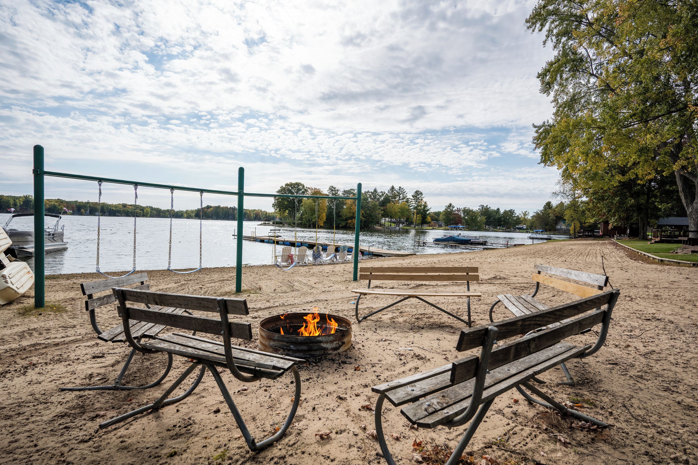 Ein Strand mit Feuerstelle und Bänken, mit Blick auf einen See mit Booten.