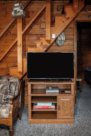 A wooden entertainment unit with a flat-screen TV, a remote control, and board games.