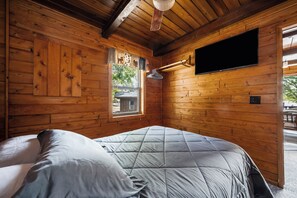 A wooden cabin room with a bed, a window, and a mounted television.
